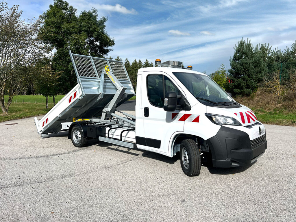 Camion benne blanc avec bras hydraulique levé, ciel bleu en arrière-plan.